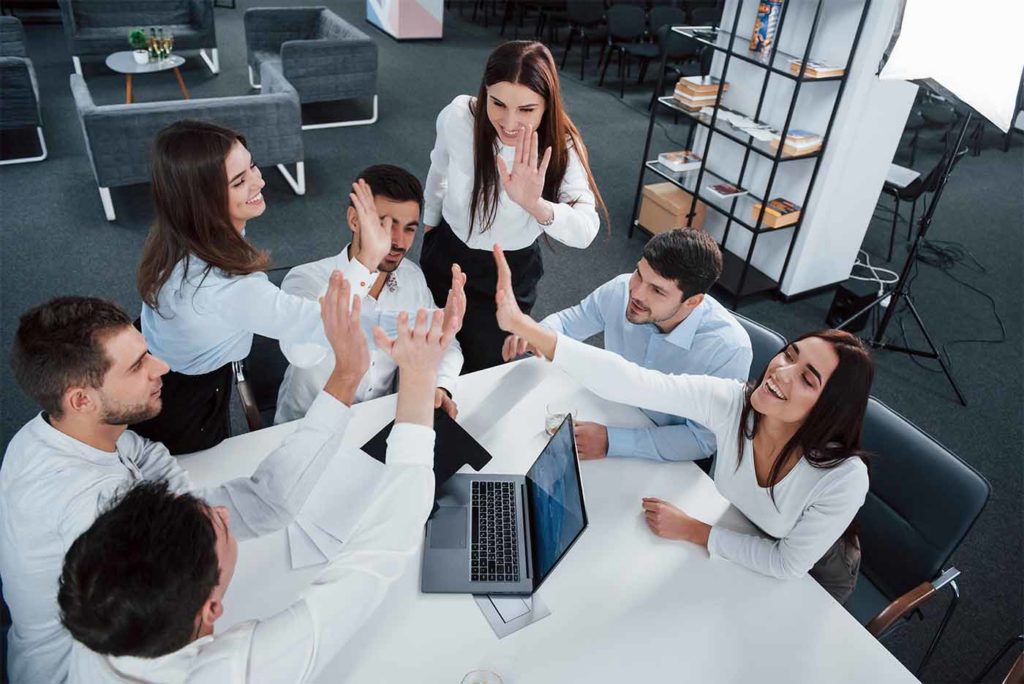 Giving high five to each other. Top view of office workers in classic wear sitting near the table using laptop and documents