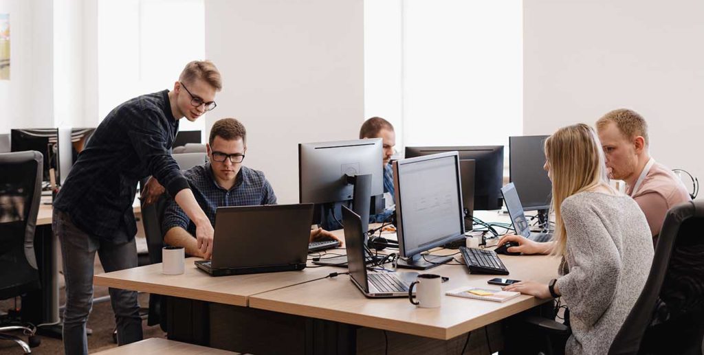 Full concentration at work. Group of young business people working and communicating while sitting at the office desk together with colleagues sitting in the background