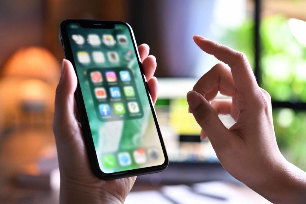 Female holding Iphone xr with icons of social media on the screen at home