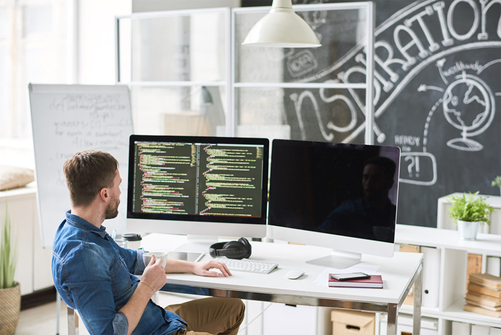 Male programmer analyzing code on two computer monitor