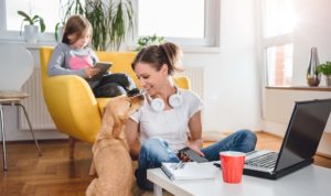 Woman sitting on the floor and Stroking dog at home while daughter sitting on the armchair and using tablet